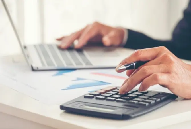 Person using a calculator and a laptop with charts on the desk, symbolizing hydraulic calculations.